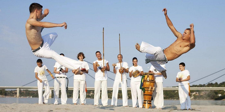Capoeiristas in roda formation performing acrobatic movements with musical instruments nearby Capoeiristas in roda formation performing acrobatic movements with musical instruments nearby