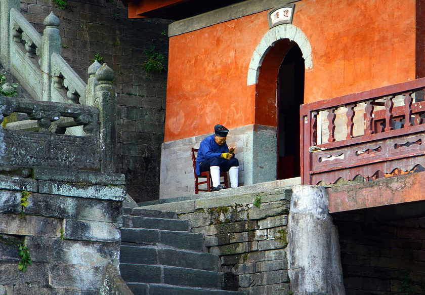 Elderly taoist monk sitting at the entrance to Purple Cloud Temple in Wudang Mountains, Hubei province Elderly taoist monk Purple Cloud Temple | Fighting Arts Health Lab