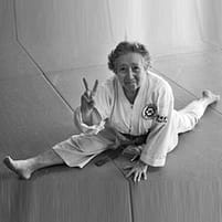 Older woman in a gi doing full splits on the mat, showing flexibility from martial arts training as you age