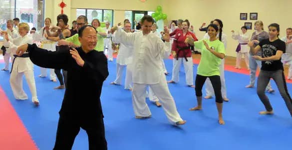 Students of all ages following a Tai Chi instructor in a dojo Students of all ages following a Tai Chi instructor in a dojo