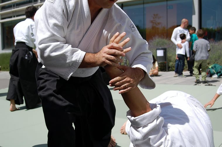 Aikido Nikkyo Grip Makunin Pixabay Aikido instructor in a white gi and black hakama applying a wrist lock to a partner who is bent toward the mat