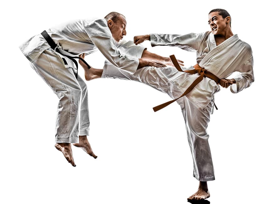 Karate student in an orange belt landing a kick to the midsection of a black belt